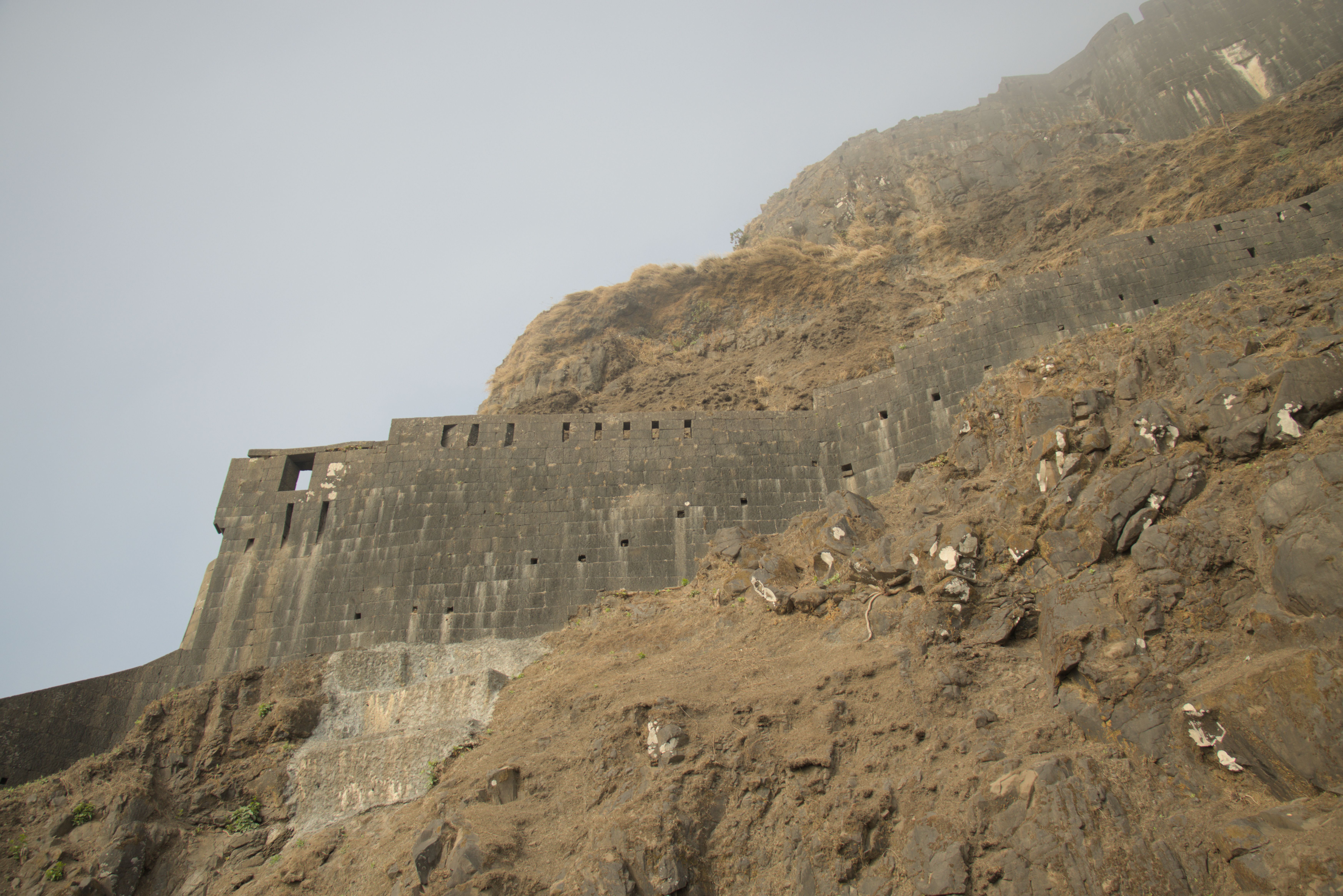 Fog lifting looking up at Lohagad Fort's fortifications.